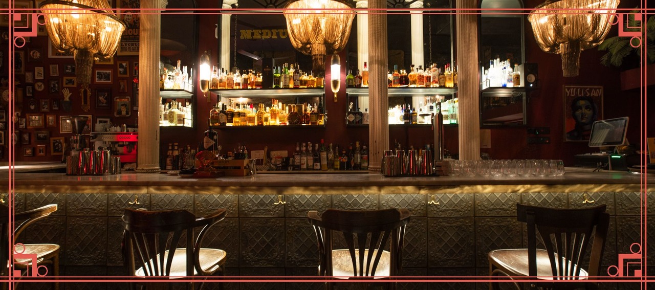 Barra iluminada de Medium Club en Malasaña, Madrid, con botellas de licores, lámparas doradas y decoración vintage.